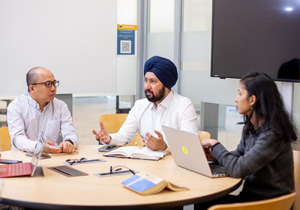 Three people at a table. One man is wearing a turban. 